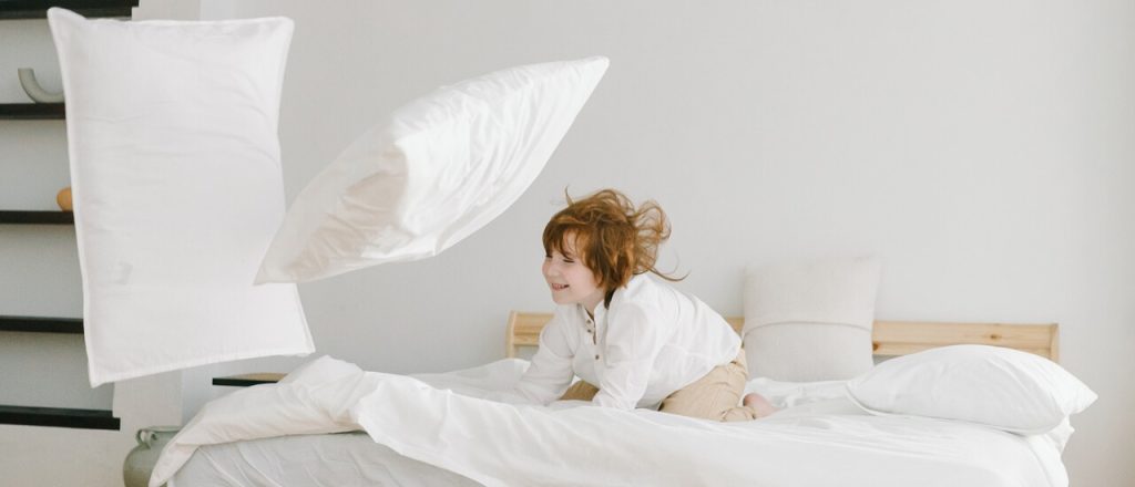 A child joyfully playing with colorful pillows on a bed in a modern designed house.