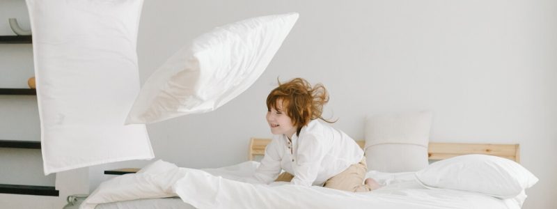 A child joyfully playing with colorful pillows on a bed in a modern designed house.