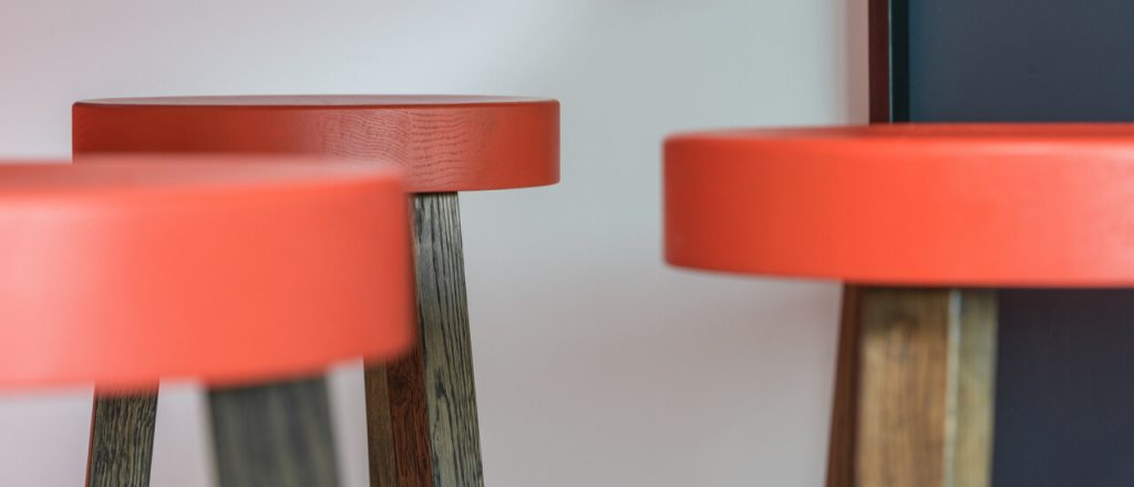 Three stools with red leather seats, emphasizing sustainable construction in their design.