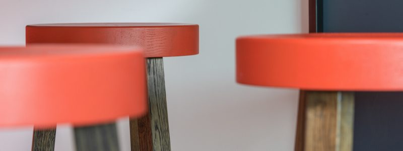 Three stools with red leather seats, emphasizing sustainable construction in their design.