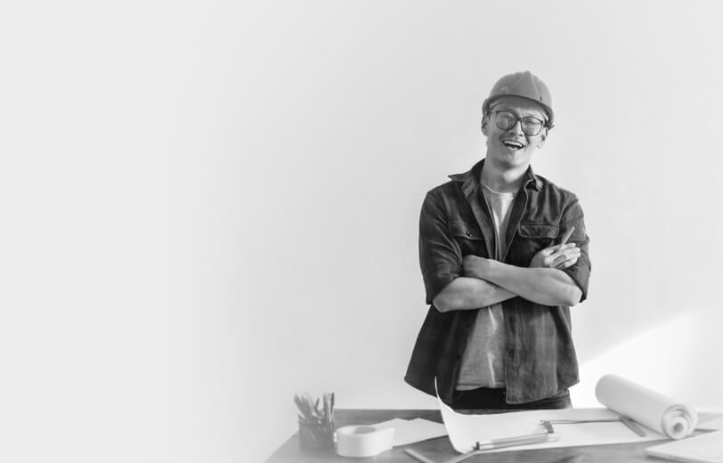 A man in a hard hat stands by a table displaying construction plans, focused on the project ahead.