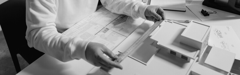 A man is focused on an architecture plan while working at a desk, surrounded by drafting tools and materials.